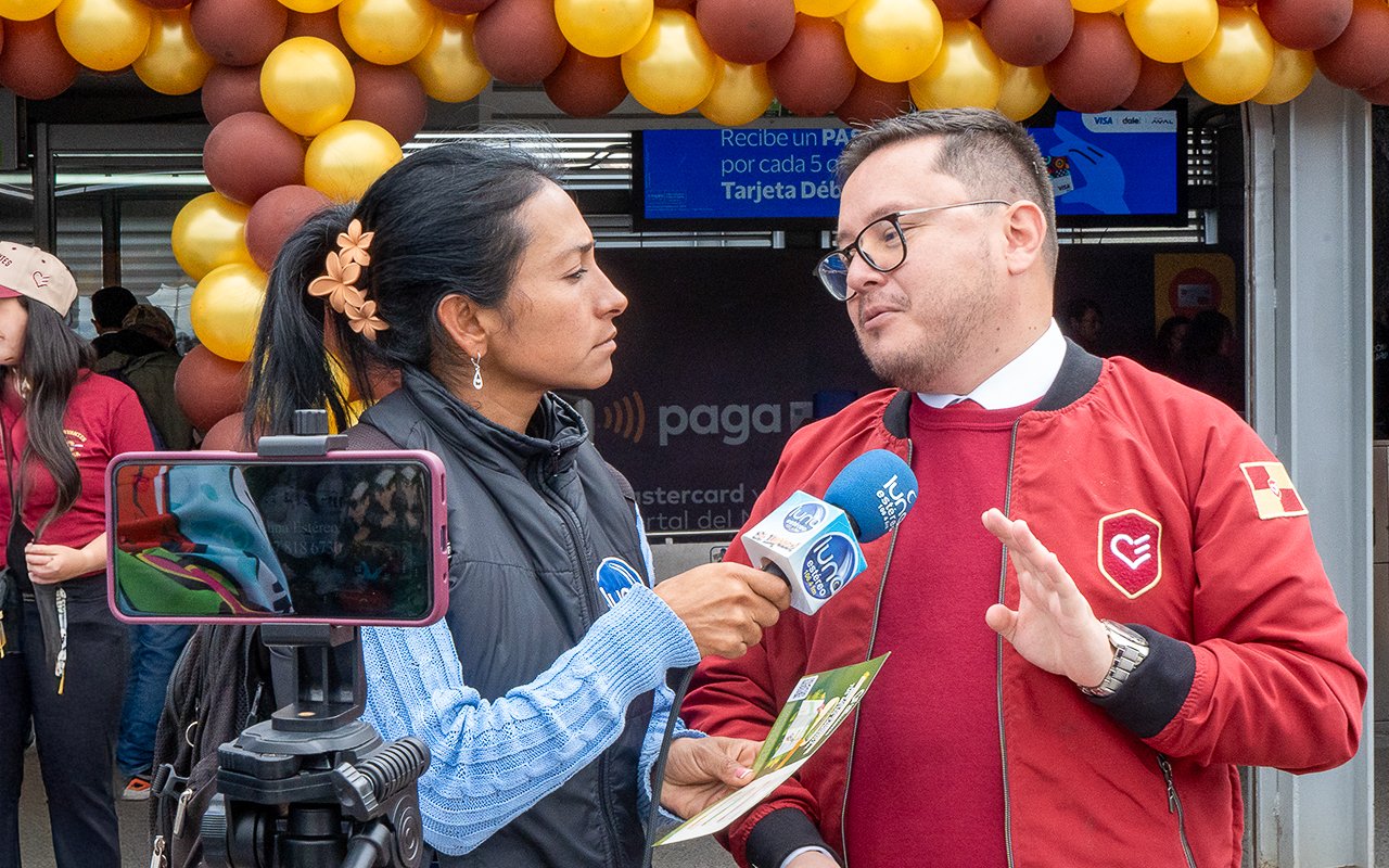 Entrevista de una reportera de Luna Stereo a un directivo de UNICERVANTES frente a la entrada decorada del Portal Norte durante el evento de alianza con TransMilenio.