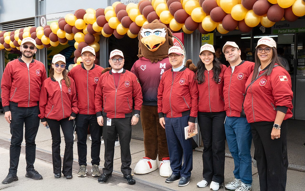 Equipo directivo de UNICERVANTES junto a Magnus, la mascota institucional, frente al Portal Norte decorado con globos vinotinto y dorados.