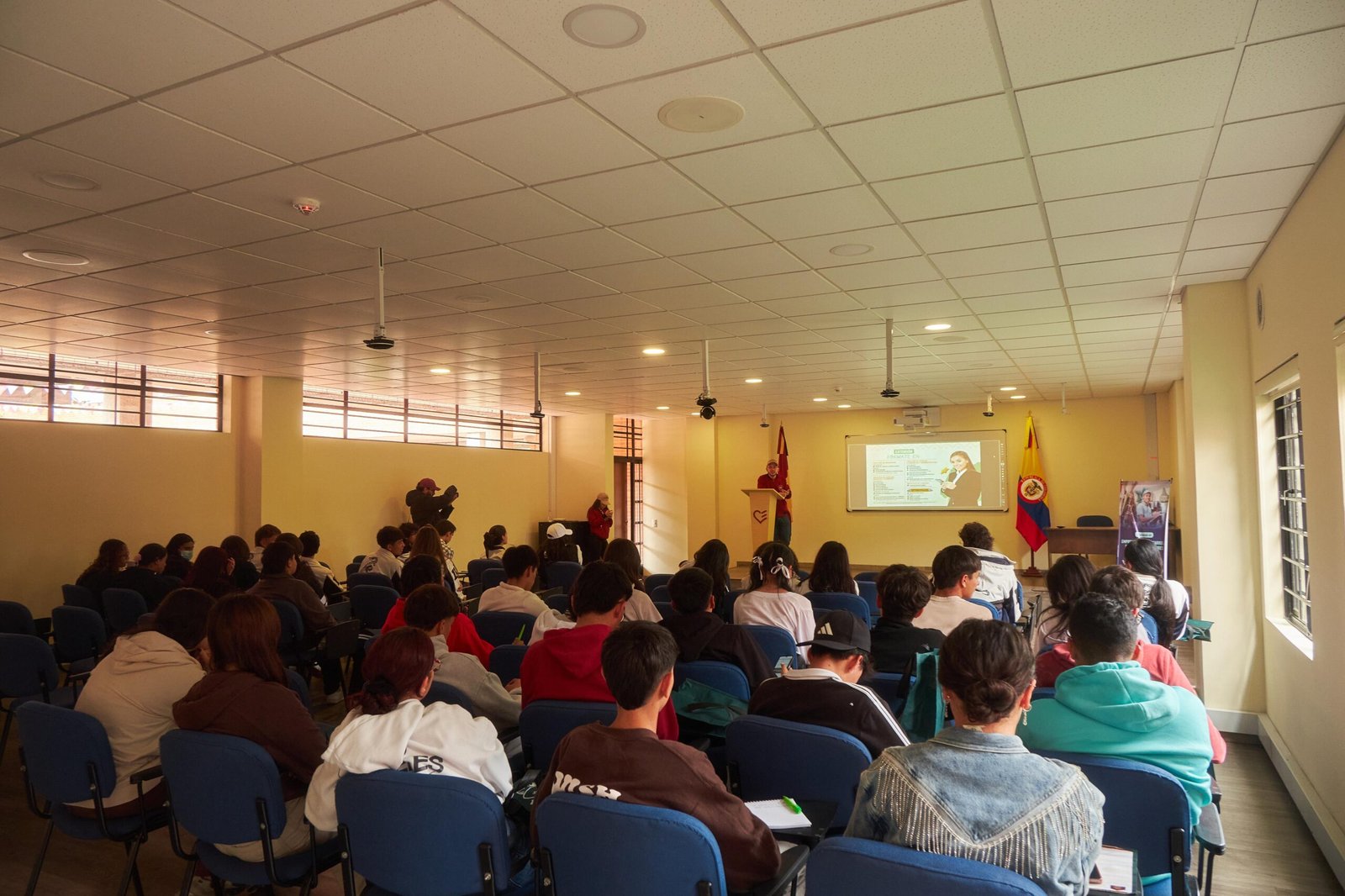 Estudiantes asisten a una charla académica durante el Brunch Fest 2025, en un aula equipada con proyector y banderas institucionales, donde se presentan programas universitarios y oportunidades profesionales.