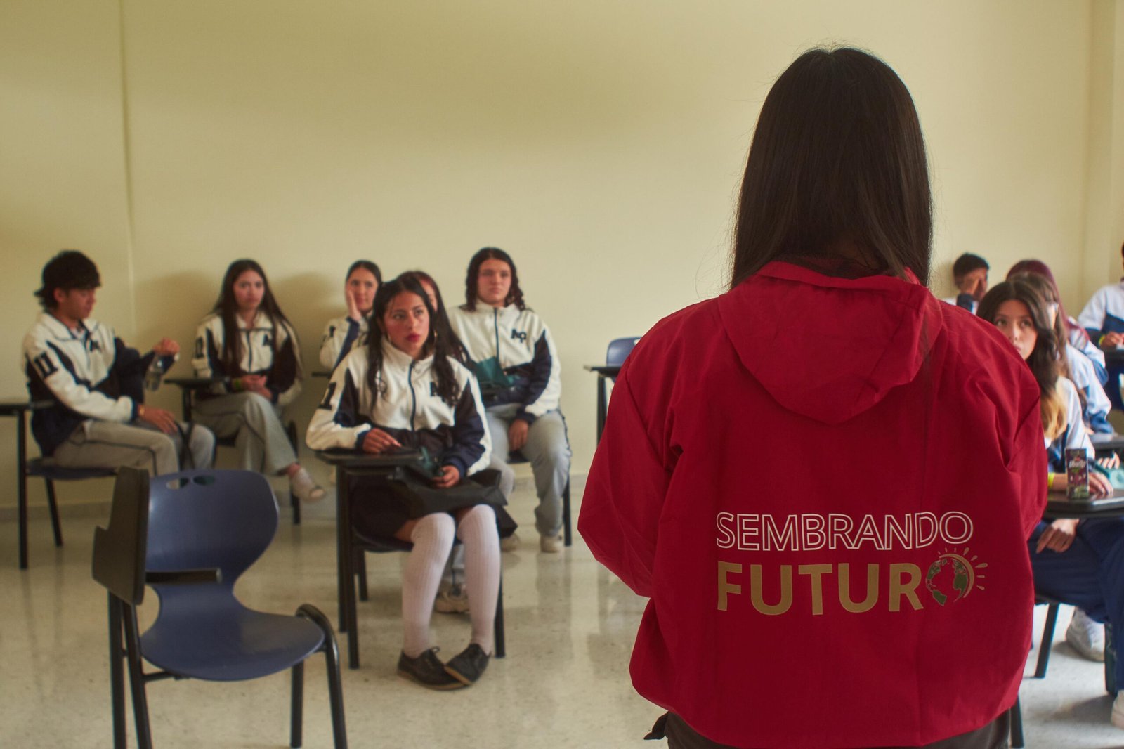 Estudiante con chaqueta roja de “Sembrando Futuro” frente a un grupo de jóvenes en un aula del Brunch Festival de Unicervantes.